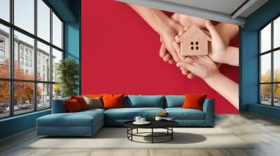 Hands of family with small house on color background Wall mural