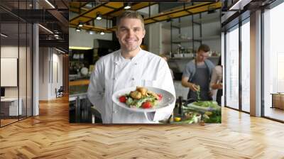 Handsome male chef holding plate with prepared dish during cooking classes Wall mural