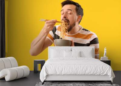 Handsome man eating Chinese noodles on yellow background Wall mural