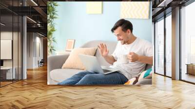 Handsome man with laptop drinking coffee at home Wall mural