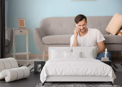 Handsome man with laptop talking by phone at home Wall mural