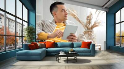 Handsome man with warm plaid using tablet computer at home Wall mural