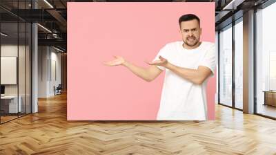 Handsome worried young man showing something on pink background Wall mural