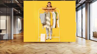 Handsome young happy man and rack with stylish clothes on yellow background Wall mural