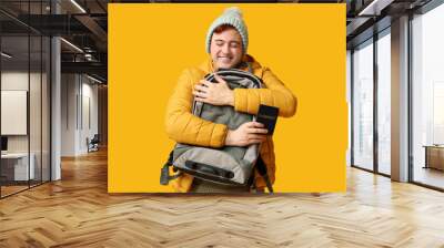 Handsome young happy man with backpack and passport on yellow background. Winter vacation concept Wall mural