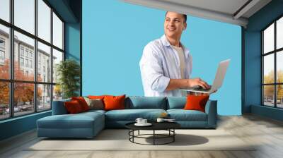 Handsome young happy man with laptop on blue background Wall mural