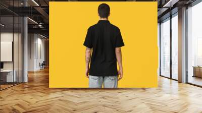 Handsome young man in stylish black t-shirt on yellow background, back view Wall mural