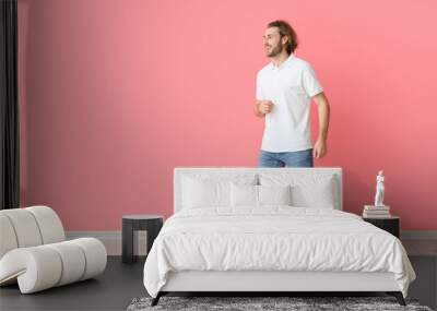 Handsome young man in stylish polo shirt and jeans on pink background Wall mural