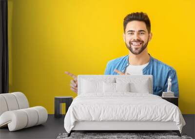 Handsome young man pointing at something on color background Wall mural