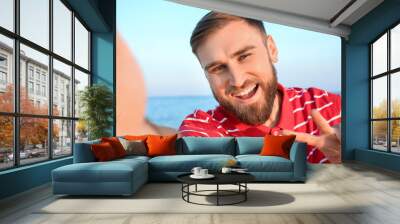 Handsome young man taking selfie on sea beach Wall mural