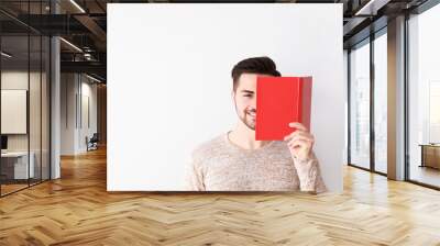 Handsome young man with book on light background Wall mural