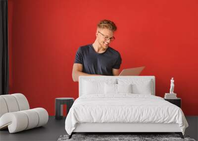 Handsome young man with laptop on color background Wall mural