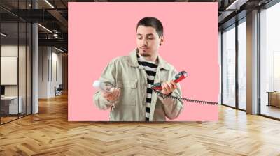 Handsome young man with two phone receivers on pink background Wall mural