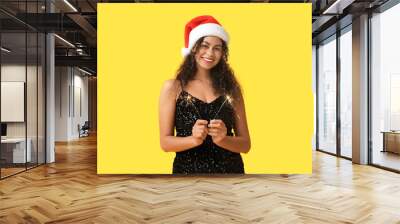 Happy African-American woman in Santa hat and with Christmas sparklers on yellow background Wall mural