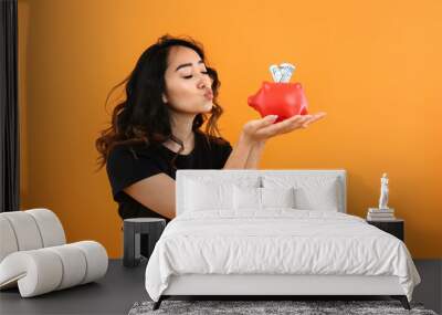 Happy Asian woman with piggy bank on color background Wall mural