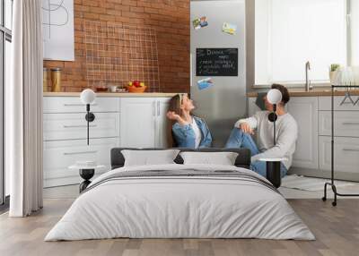 Happy couple sitting on floor near refrigerator in kitchen Wall mural