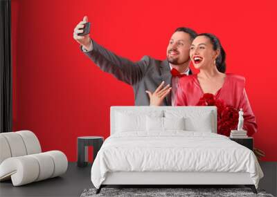 Happy engaged couple with flowers taking selfie on red background Wall mural