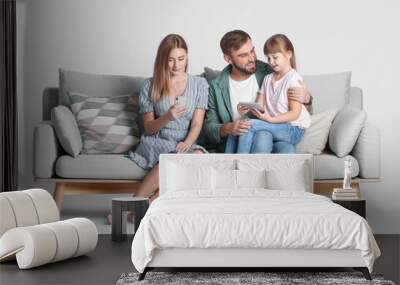 Happy family with modern devices on sofa against light background Wall mural