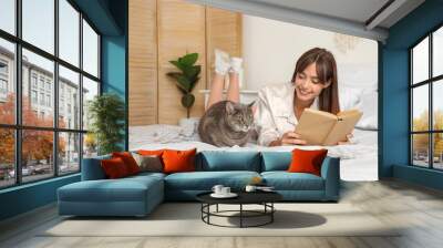 Happy female student with cute cat reading books at home Wall mural