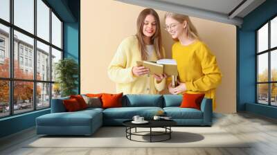 Happy female students reading book  on pale yellow background Wall mural