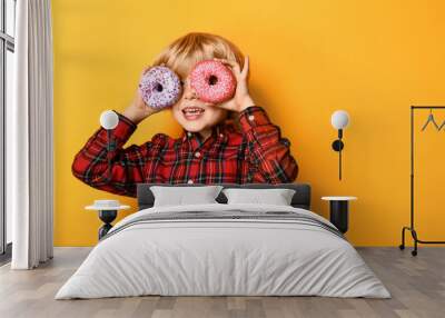 Happy little boy with tasty donuts on color background Wall mural