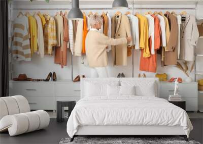 Happy mature female stylist choosing clothes in studio Wall mural