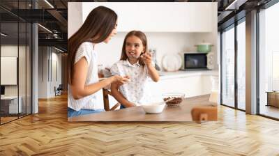 Happy mother with her little daughter having breakfast in kitchen Wall mural