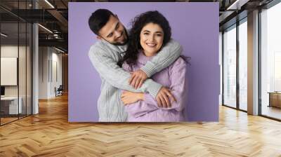 Happy young couple in warm sweaters on lilac background Wall mural