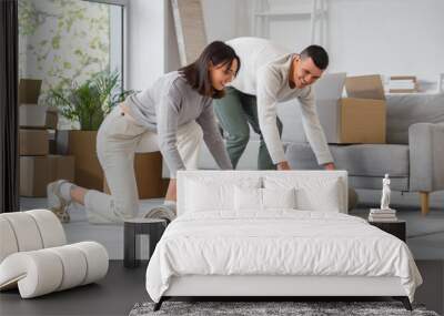 Happy young couple rolling carpet in room on moving day Wall mural