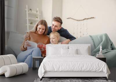 Happy young family reading fashion magazine while sitting on sofa at home Wall mural