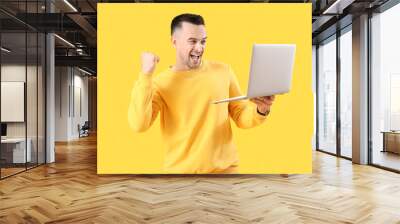 Happy young man with laptop on yellow background Wall mural