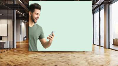 Happy young man with mobile phone on light color background with space for text Wall mural