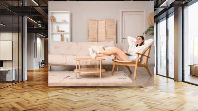 Happy young woman relaxing in wooden armchair at home Wall mural