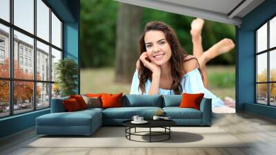 Happy young woman resting on plaid in park Wall mural