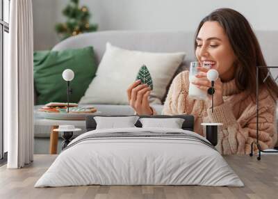 Happy young woman with gingerbread cookie and glass of milk at home Wall mural