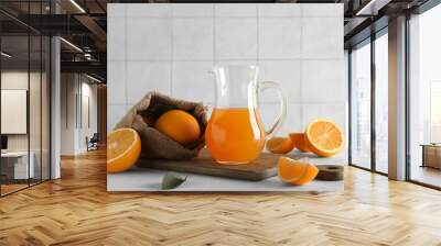 Jug of fresh orange juice and sack bag with fruits on white table Wall mural