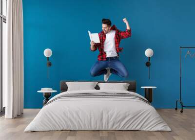 Jumping young man with book on color background Wall mural