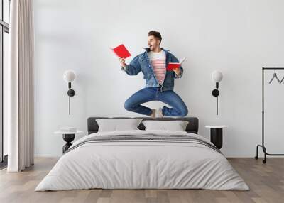 Jumping young man with books on light background Wall mural