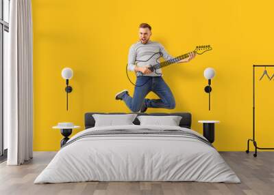 Jumping young man with drawn guitar on color background Wall mural