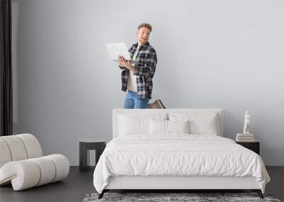 Jumping young man with laptop on light background Wall mural