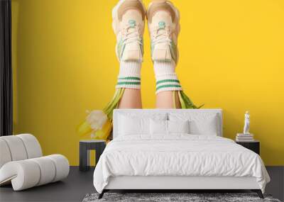 Legs of beautiful young woman in sneakers with tulips on yellow background Wall mural