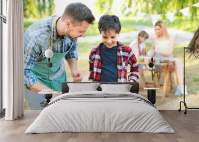 Little boy with father cooking tasty food on barbecue grill outdoors Wall mural