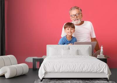 Little boy with his grandfather using laptop on red background Wall mural