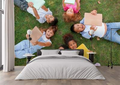 Little children with books lying on green grass in park Wall mural