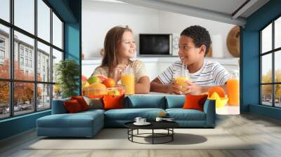 Little children with glasses of fresh citrus juice sitting at table in kitchen Wall mural