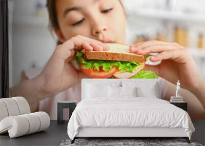 Little girl eating tasty sandwich in kitchen, closeup Wall mural