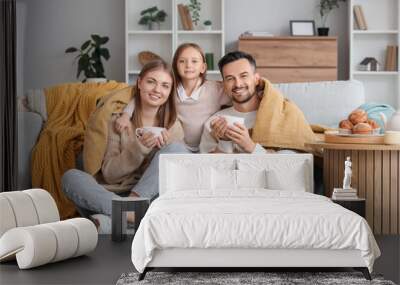 Little girl hugging her parents with warm plaid and cups of tea at home Wall mural