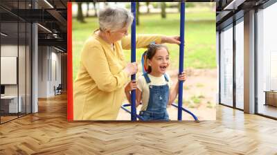 Little girl with her grandma playing on swings in park Wall mural