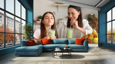 Little girl with her mother drinking green smoothie at table in kitchen Wall mural