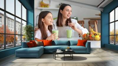 Little girl with her mother drinking green smoothie at table in kitchen Wall mural